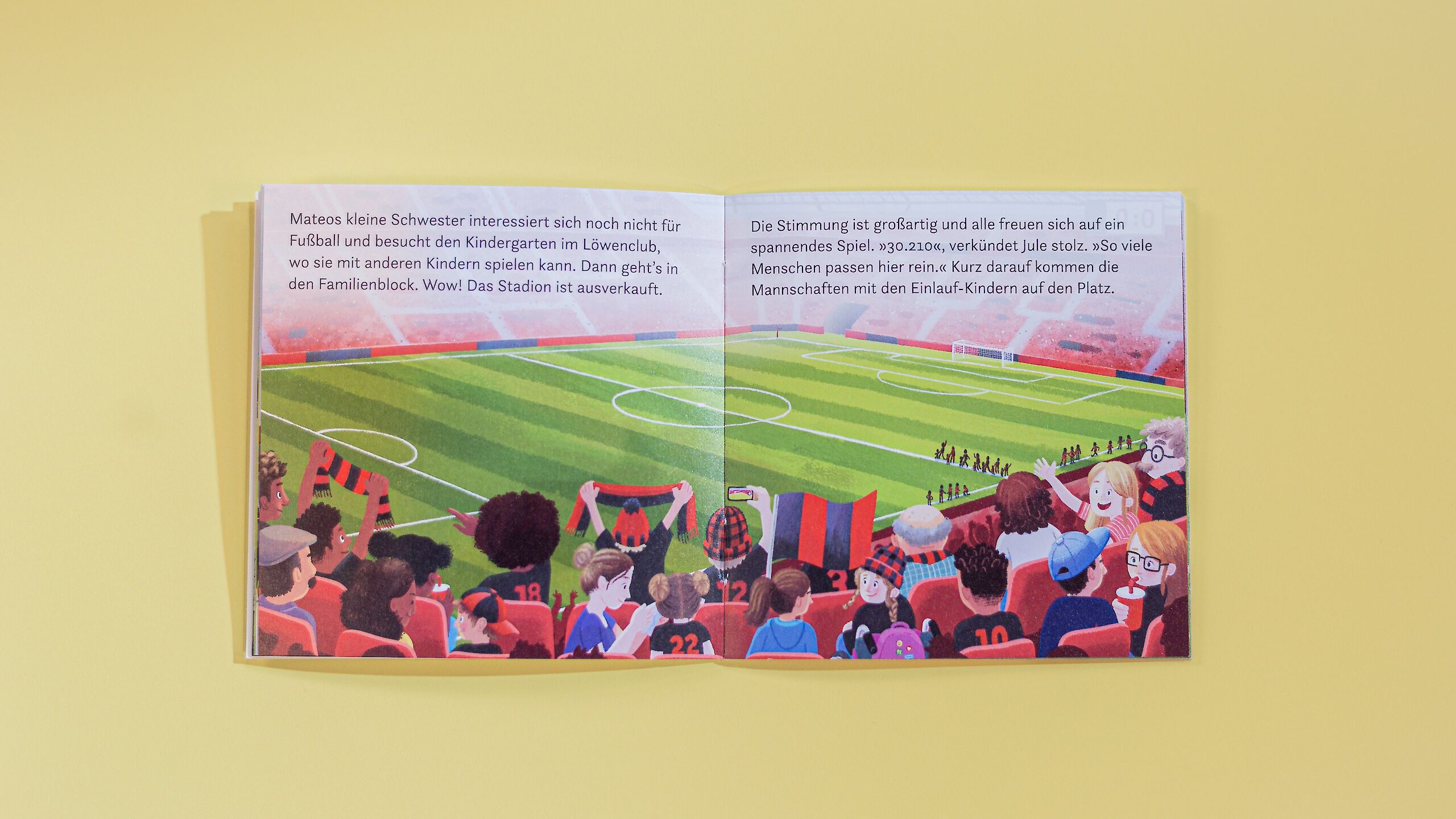 Das Bild zeigt eine aufgeschlagene Seite eines Pixi-Buches. Auf der Illustration ist ein großes Fußballstadion zu sehen, das voller Zuschauer ist, die bunte Schals und Trikots tragen. Einige halten Fahnen oder jubeln begeistert. Auf dem Spielfeld laufen die Mannschaften mit Einlaufkindern auf den Platz. Darüber befindet sich Text, der die Szene beschreibt.