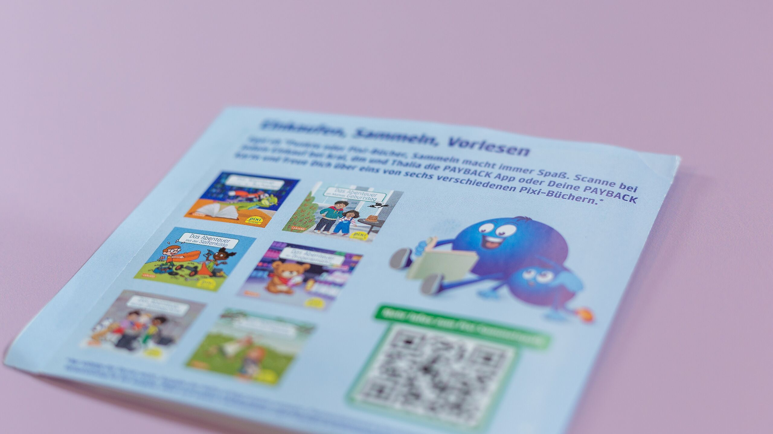 Das Bild zeigt die Rückseite der Überraschungspackung der Pixi-Bücher mit der Überschrift „Einkaufen, Sammeln, Vorlesen“. Es sind sechs verschiedene Pixi-Buch-Cover abgebildet, darunter „Das Abenteuer mit der Seifenkiste“. Rechts ist ein blauer PAYBACK-Charakter mit einem Buch zu sehen, darunter ein QR-Code.