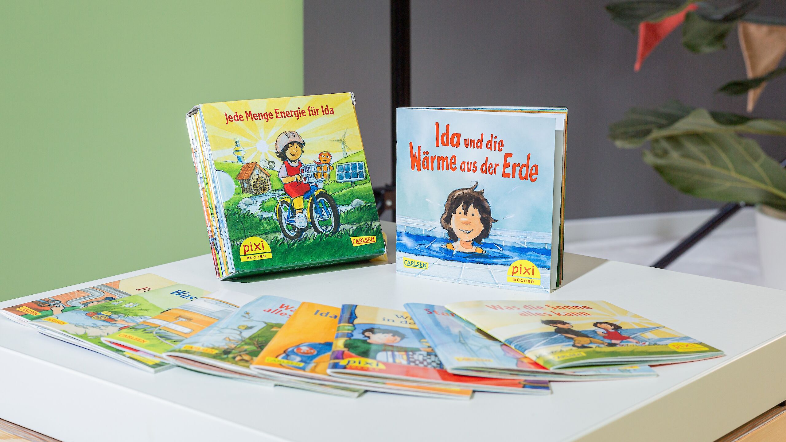 Das Bild zeigt mehrere Pixi-Bücher, die auf einem Tisch ausgestellt sind. Zwei Bücher stehen aufrecht: „Jede Menge Energie für Ida“ und „Ida und die Wärme aus der Erde“. Weitere Pixi-Bücher liegen davor.