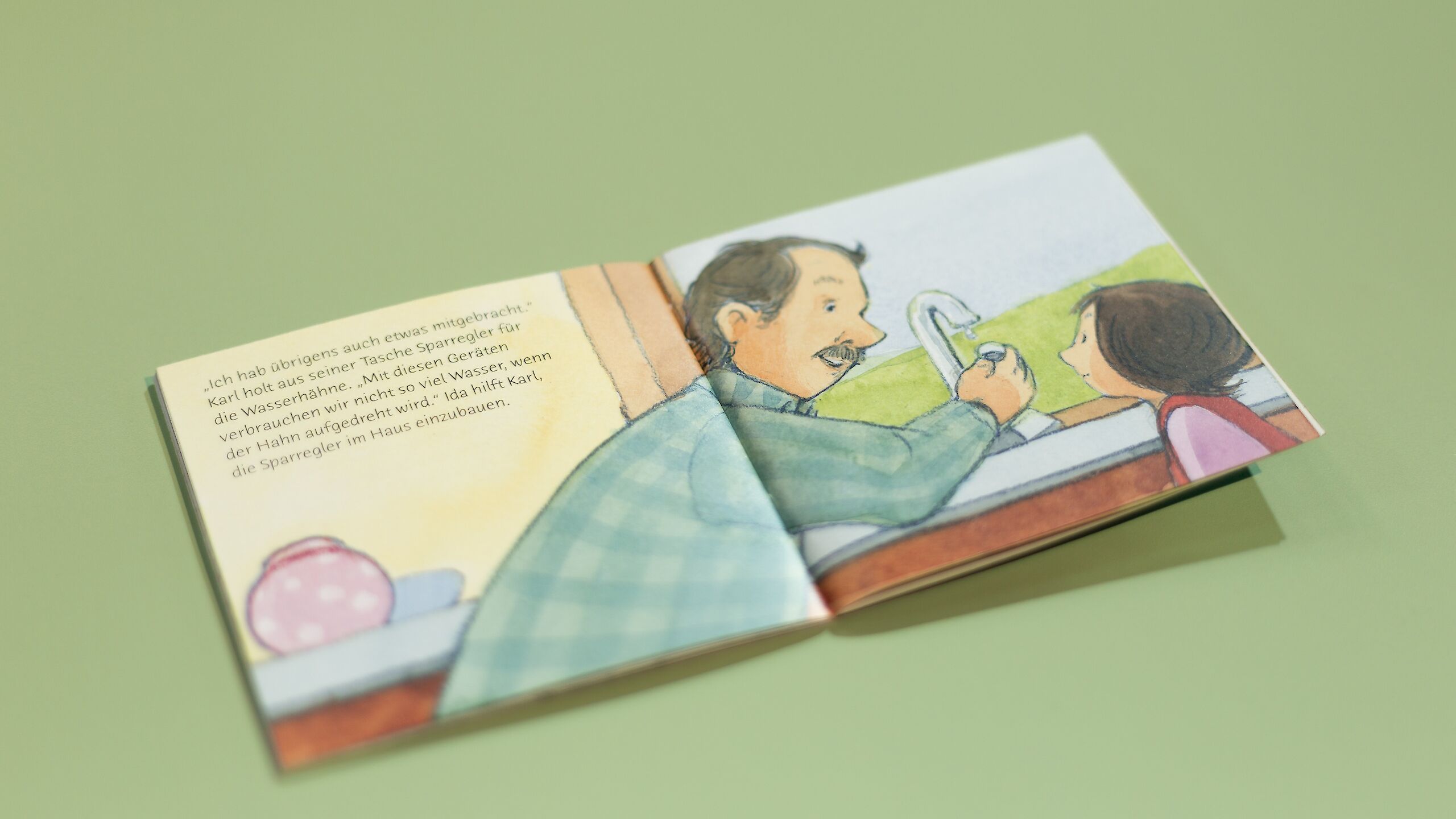 Ein aufgeschlagenes Pixi-Buch liegt auf einem grünen Tisch. Auf der rechten Seite ist ein Mann an einem Wasserhahn zu sehen, während ein Kind ihn anschaut.