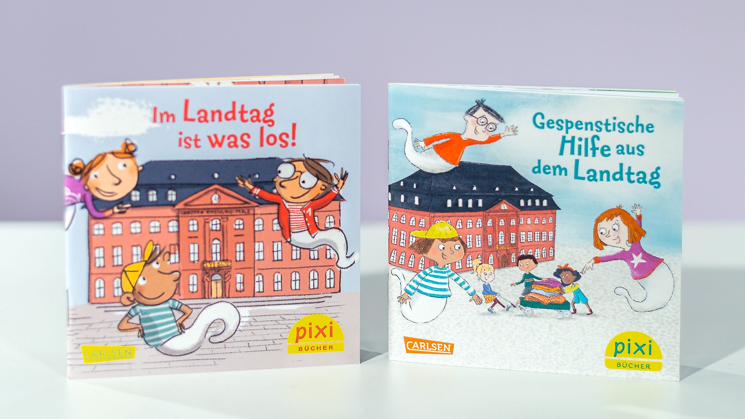 Das Bild zeigt zwei Pixi-Bücher. Das linke Buch heißt „Im Landtag ist was los!“ und zeigt Kinder als Geister vor einem großen Gebäude. Das rechte Buch heißt „Gespenstische Hilfe aus dem Landtag“ und zeigt Geister, die Menschen helfen. Beide Bücher haben bunte, fröhliche Cover.