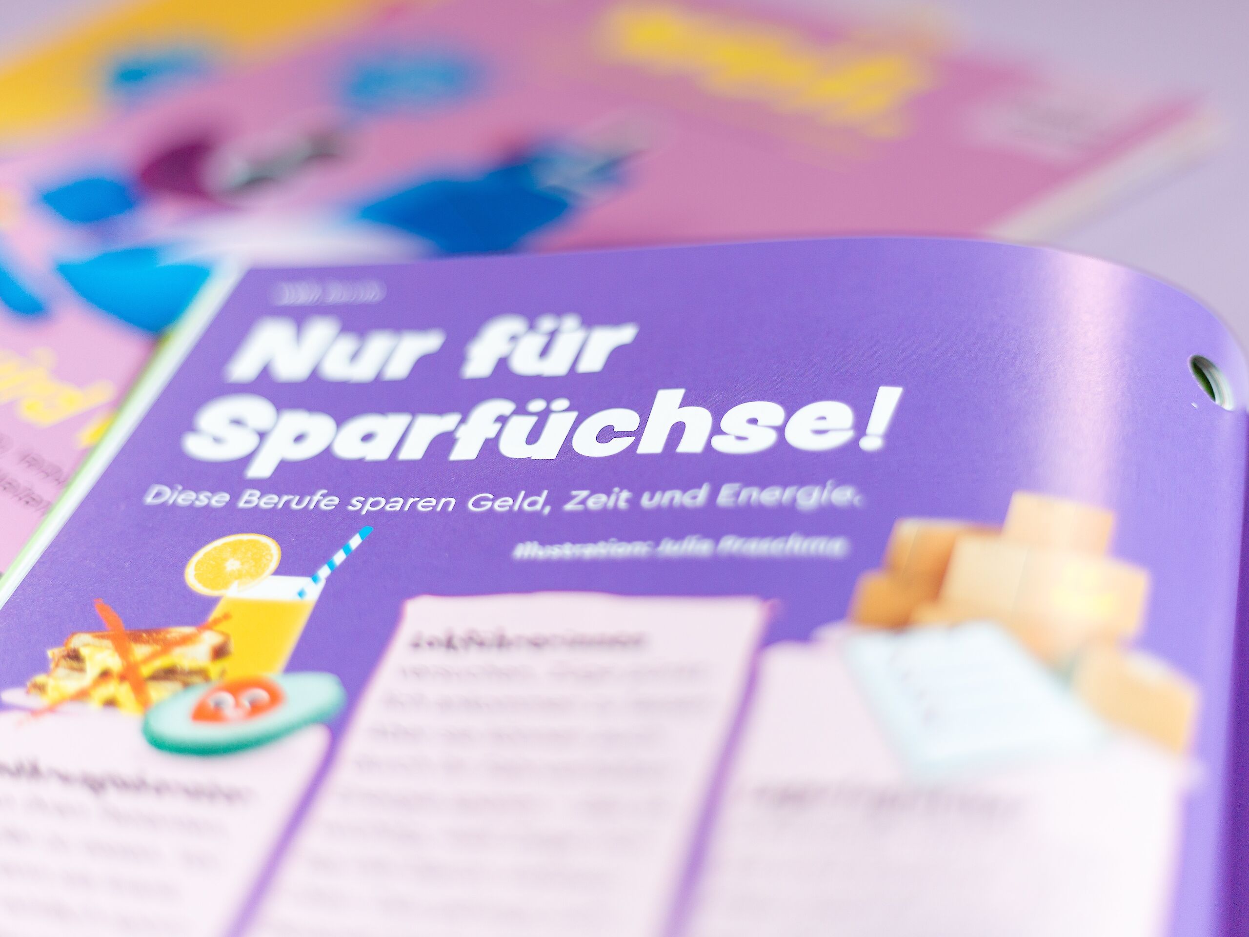 Das Bild zeigt eine Seite mit der Überschrift „Nur für Sparfüchse!“ auf lila Hintergrund. Darunter steht, dass bestimmte Berufe Geld, Zeit und Energie sparen. Es sind kleine Illustrationen von Essen, Getränken und Paketen zu sehen. Im Hintergrund liegen bunte Hefte.